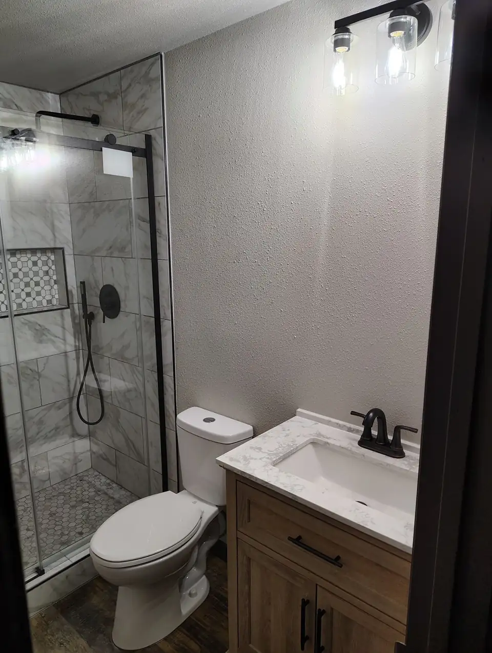 Walk-in shower with marble-look wall tile, mosaic niche and black fixtures, finished by a tile contractor in Ruidoso, NM